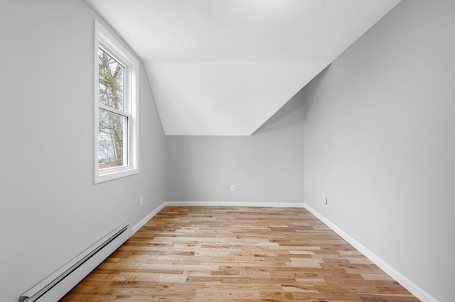 additional living space featuring baseboard heating, light wood-style floors, baseboards, and vaulted ceiling