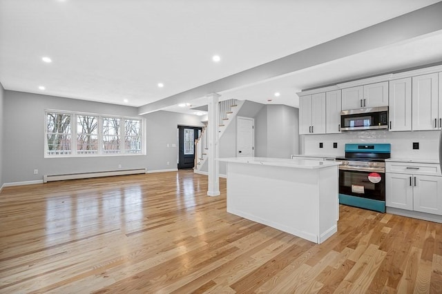 kitchen with light wood-type flooring, a kitchen island, baseboard heating, stainless steel appliances, and open floor plan