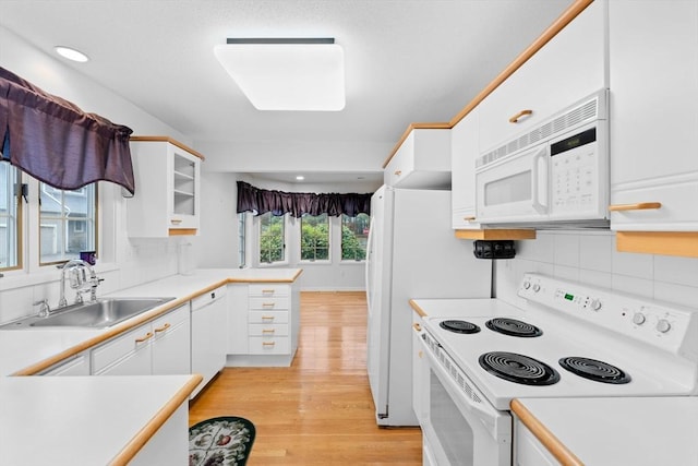 kitchen featuring light countertops, white cabinets, a sink, light wood-type flooring, and white appliances