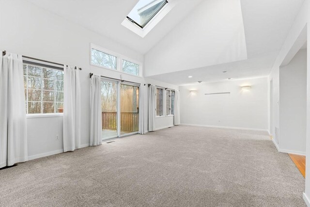 unfurnished living room featuring carpet, high vaulted ceiling, a skylight, and baseboards