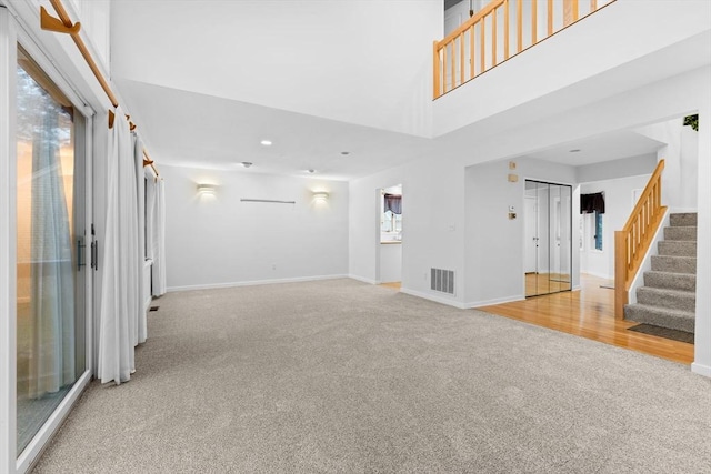 unfurnished living room with stairway, carpet, a high ceiling, and visible vents