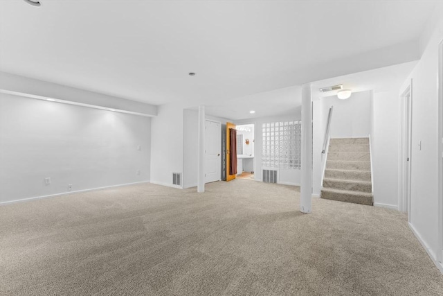 unfurnished living room with light colored carpet, visible vents, stairway, and baseboards