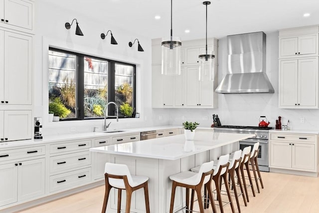 kitchen featuring a center island, wall chimney exhaust hood, stainless steel appliances, sink, and a kitchen bar