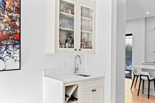 bar featuring white cabinetry, sink, light stone counters, and light hardwood / wood-style flooring