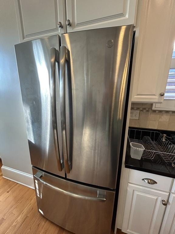 interior details with light wood finished floors, white cabinets, decorative backsplash, dark countertops, and freestanding refrigerator