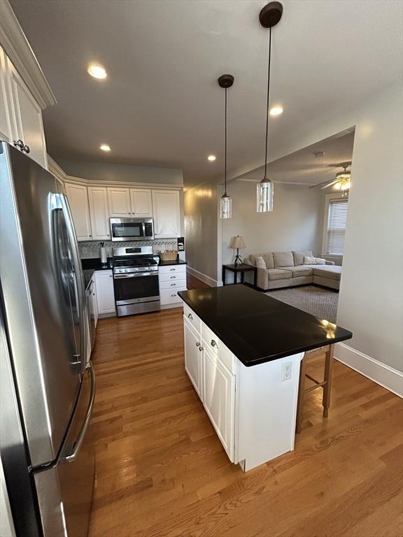 kitchen featuring stainless steel appliances, dark countertops, open floor plan, and white cabinets