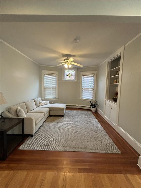 living area with baseboards, built in features, a ceiling fan, wood finished floors, and baseboard heating