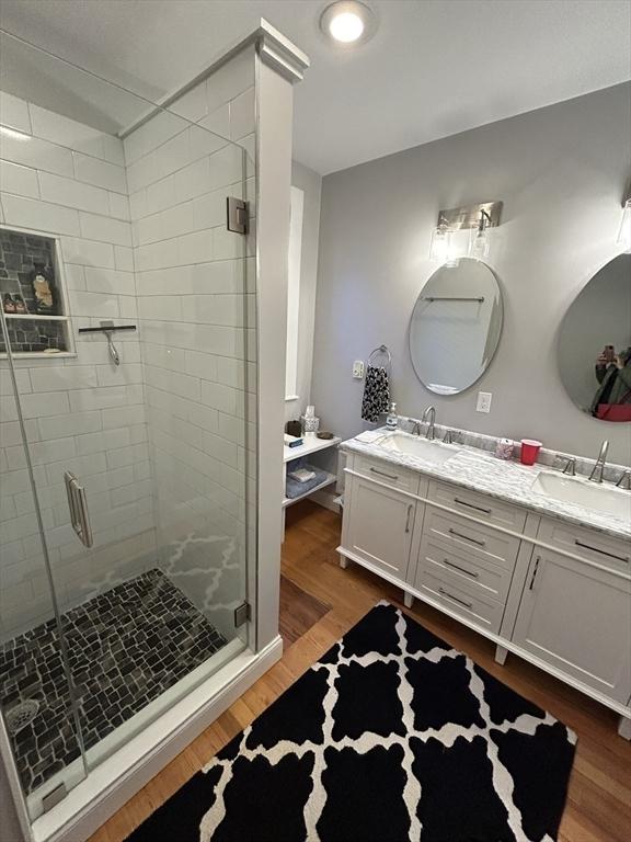 bathroom featuring double vanity, wood finished floors, a sink, and a shower stall