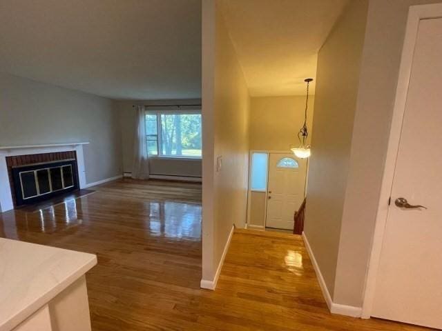 entryway featuring a brick fireplace, a baseboard radiator, baseboards, and wood finished floors