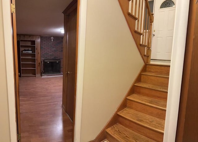 stairway with a brick fireplace and wood finished floors