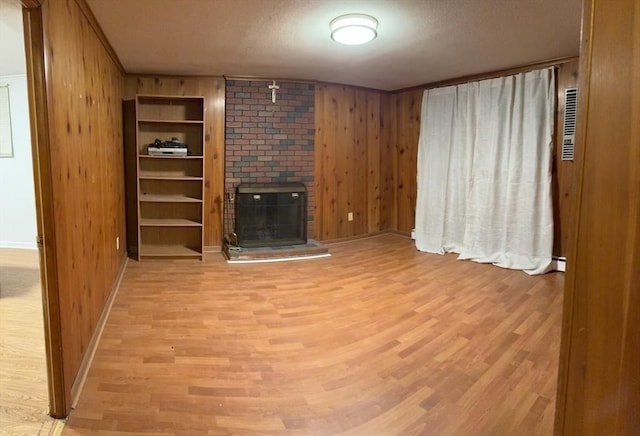 unfurnished living room featuring wood walls, a brick fireplace, and wood finished floors