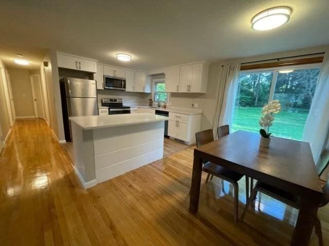 kitchen with light wood-style flooring, stainless steel appliances, white cabinets, light countertops, and a center island