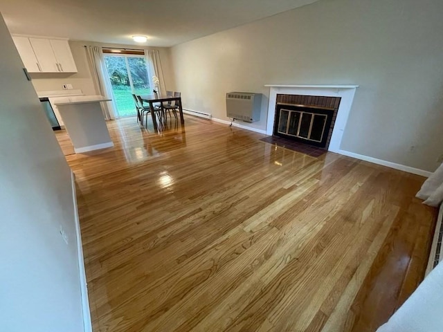 unfurnished living room with heating unit, light wood finished floors, a brick fireplace, and baseboards