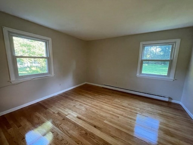 empty room featuring light wood finished floors, baseboard heating, and baseboards