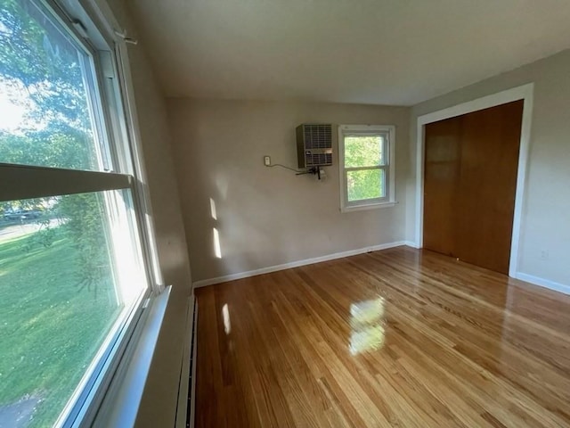 unfurnished room featuring a baseboard heating unit, baseboards, wood finished floors, and a wall mounted air conditioner