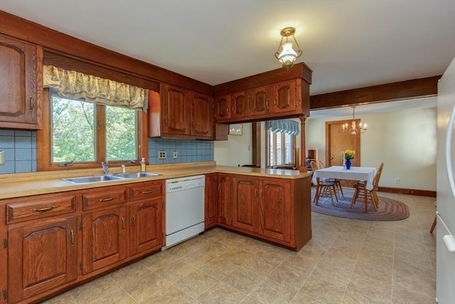kitchen featuring white dishwasher, a sink, a chandelier, backsplash, and light countertops