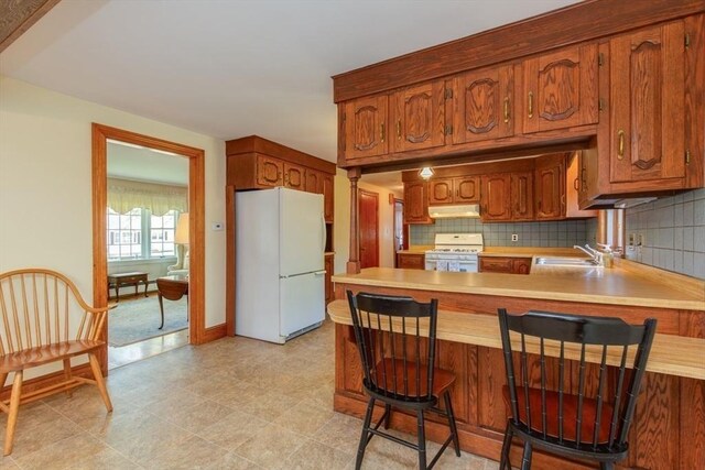 kitchen with white appliances, a sink, a peninsula, light countertops, and tasteful backsplash