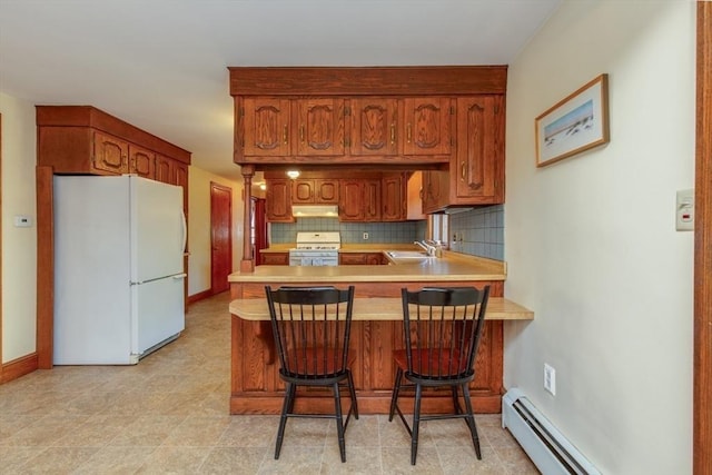 kitchen featuring white appliances, under cabinet range hood, a baseboard radiator, a peninsula, and light countertops