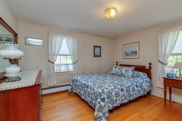 bedroom with a baseboard heating unit and light wood finished floors