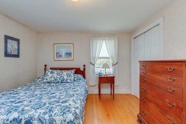 bedroom with light wood-style floors, wallpapered walls, and a closet