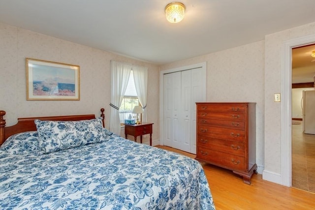 bedroom featuring wallpapered walls, light wood-style floors, a closet, and freestanding refrigerator