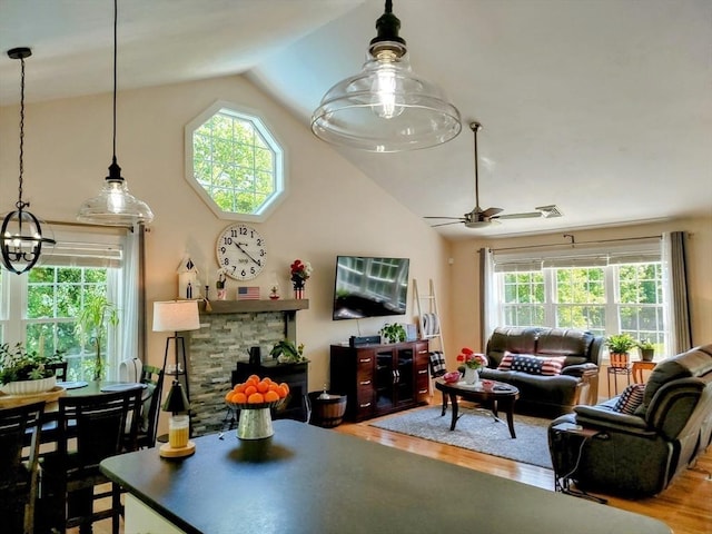 living room with vaulted ceiling, wood finished floors, healthy amount of natural light, ceiling fan, and a stone fireplace