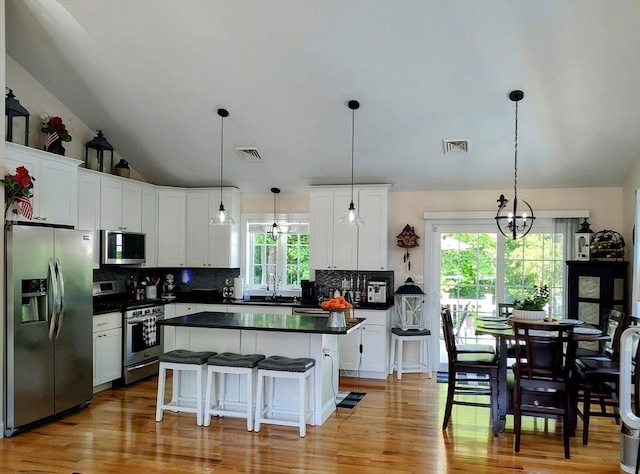 kitchen featuring appliances with stainless steel finishes, dark countertops, vaulted ceiling, tasteful backsplash, and white cabinets