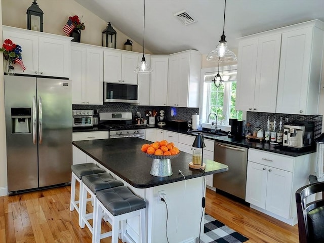 kitchen with stainless steel appliances, a sink, white cabinetry, decorative backsplash, and vaulted ceiling