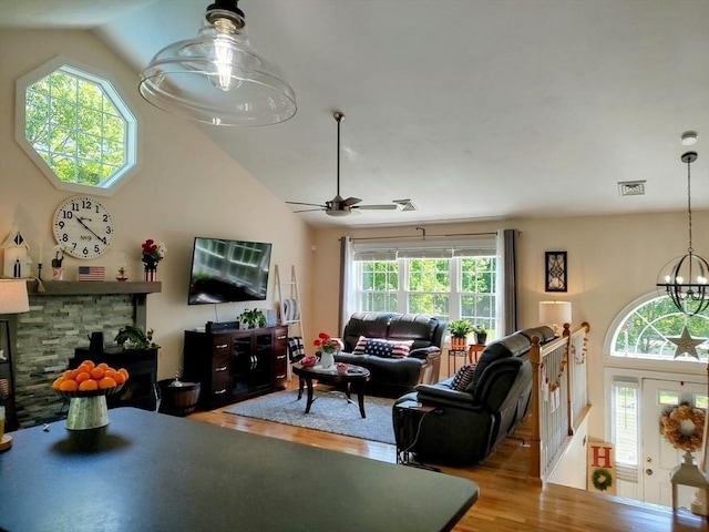 living area with wood finished floors, vaulted ceiling, a chandelier, ceiling fan, and a fireplace