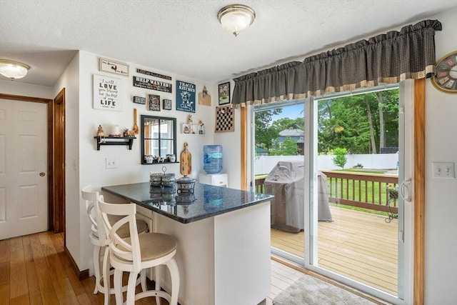 10 Manoogian Cir, Milford, MA 01757 - kitchen with hardwood / wood-style floors, a peninsula, a breakfast bar, a textured ceiling, and dark stone counters