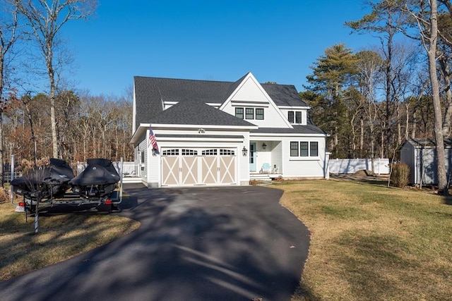 shingle-style home with an attached garage, a storage shed, fence, driveway, and a front yard