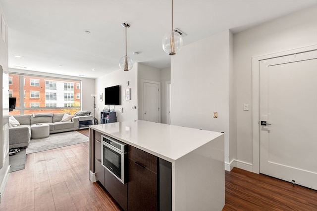 kitchen with dark brown cabinets, built in microwave, pendant lighting, dark wood-type flooring, and a kitchen island