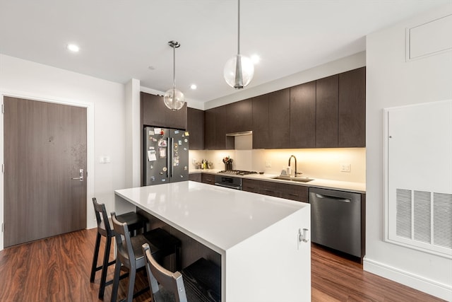 kitchen with dark hardwood / wood-style flooring, a center island, appliances with stainless steel finishes, sink, and pendant lighting