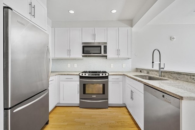 kitchen featuring appliances with stainless steel finishes, light wood-style floors, white cabinets, and a sink