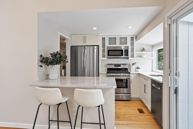 13 Long Ridge Rd, Acton, MA 01720 - kitchen featuring stainless steel appliances, a kitchen bar, decorative backsplash, white cabinetry, and glass insert cabinets