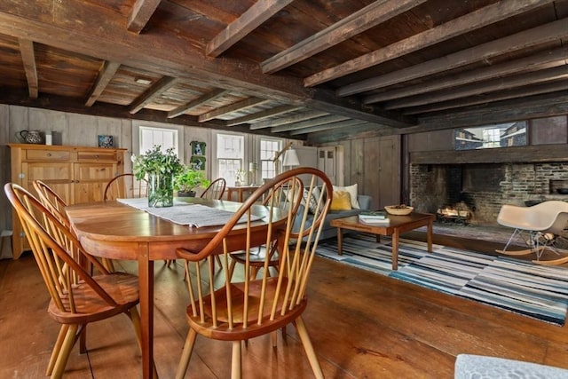 dining space with wood walls, a brick fireplace, beam ceiling, wooden ceiling, and wood-type flooring