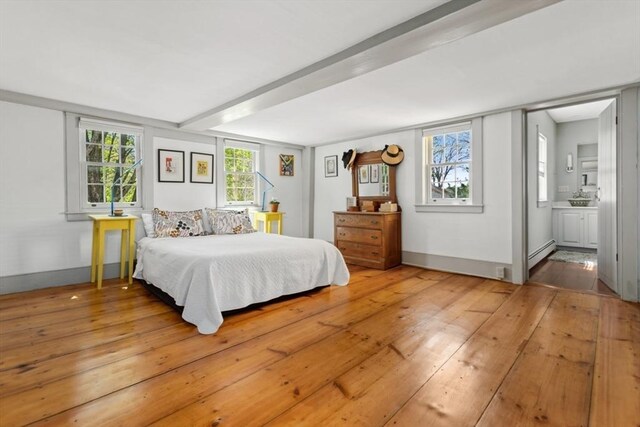 bedroom featuring baseboard heating, light wood finished floors, ensuite bath, and baseboards