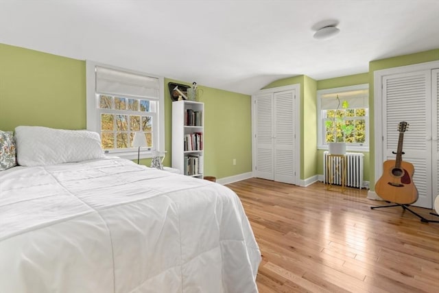 bedroom featuring multiple closets, radiator, vaulted ceiling, wood finished floors, and baseboards