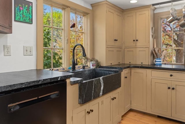 kitchen with dishwashing machine, a sink, cream cabinetry, light wood-style floors, and dark stone counters