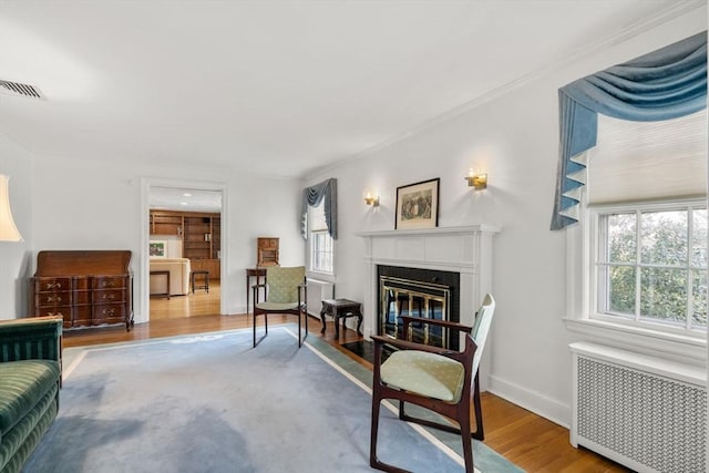 sitting room with radiator, visible vents, a glass covered fireplace, wood finished floors, and baseboards