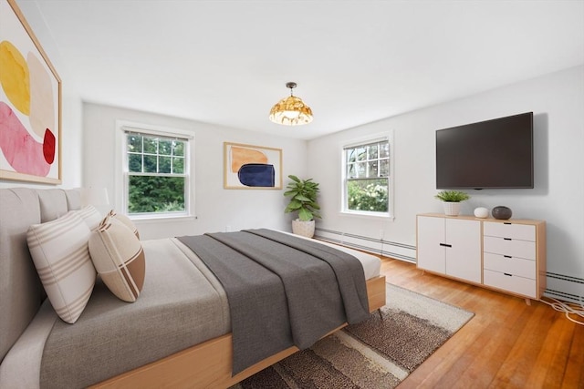 bedroom with light wood-style floors, multiple windows, and a baseboard heating unit
