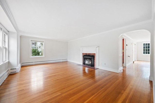 unfurnished living room featuring arched walkways, baseboard heating, a fireplace, light wood-style floors, and ornamental molding