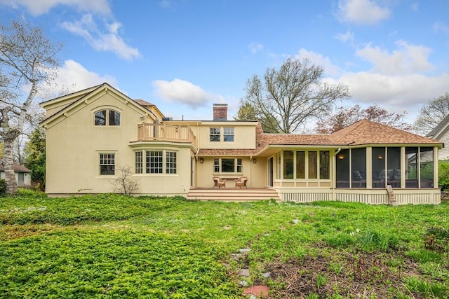 back of house featuring a balcony, stucco siding, a chimney, a sunroom, and a yard