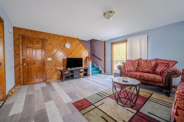living room featuring stairway, light wood finished floors, wooden walls, and an accent wall
