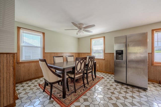 dining area with wainscoting, wooden walls, healthy amount of natural light, a ceiling fan, and light flooring