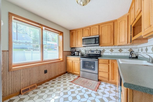 kitchen featuring appliances with stainless steel finishes, a sink, light brown cabinets, a wainscoted wall, and baseboards