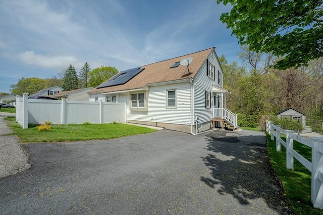 back of property with a shingled roof, roof mounted solar panels, and asphalt driveway
