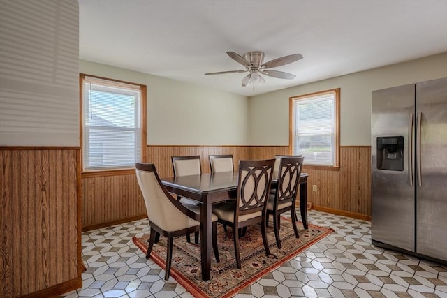 dining space featuring wainscoting, wood walls, ceiling fan, light flooring, and baseboards