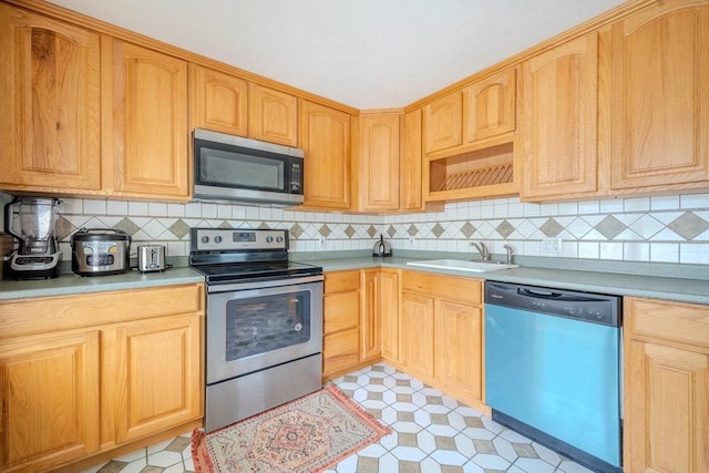 kitchen with stainless steel appliances, a sink, light brown cabinets, and tasteful backsplash
