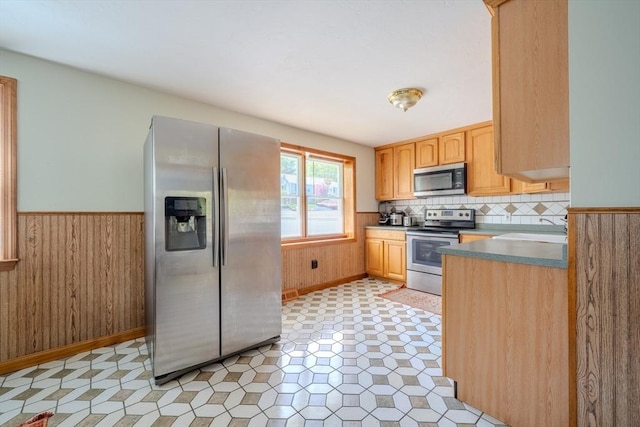 kitchen with appliances with stainless steel finishes, a sink, wainscoting, light brown cabinets, and wood walls